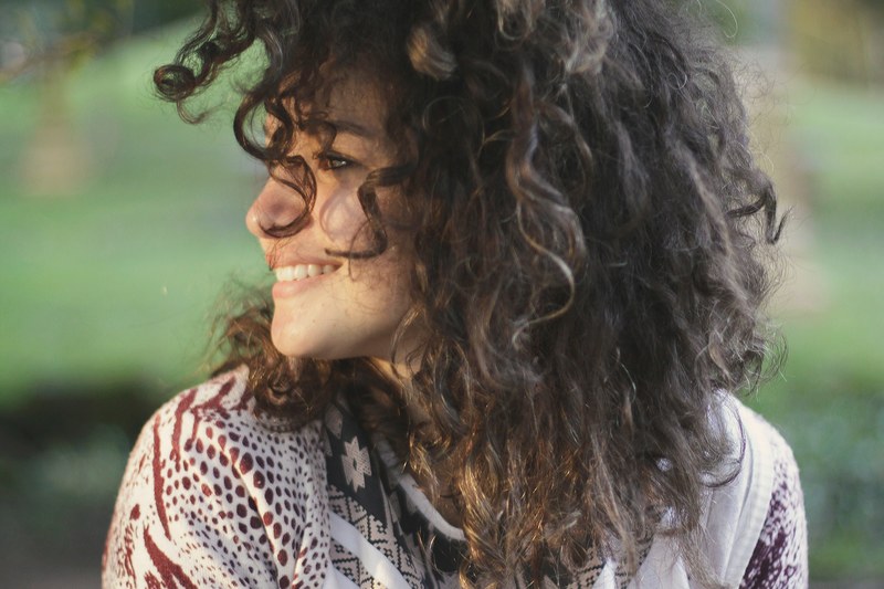 a smiling young woman with dark curly hair, curly haired woman 4k