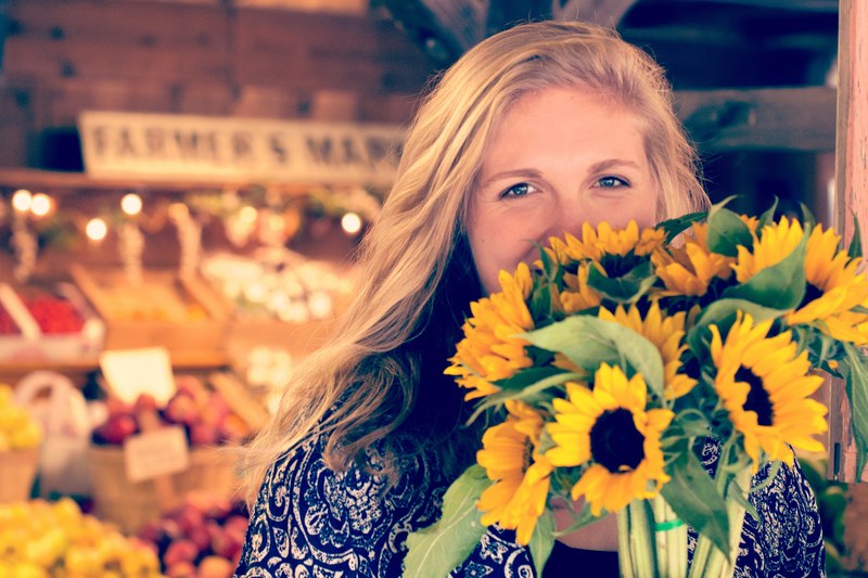 a woman in front of produce at avila valley barn holding a bouquet of sunflowers, woman with flowers in market 4k