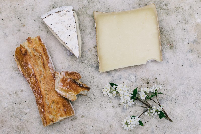 an overhead shot of a baguette two pieces of cheese and branchlet with small white flowers, picnicking at versailles 4k