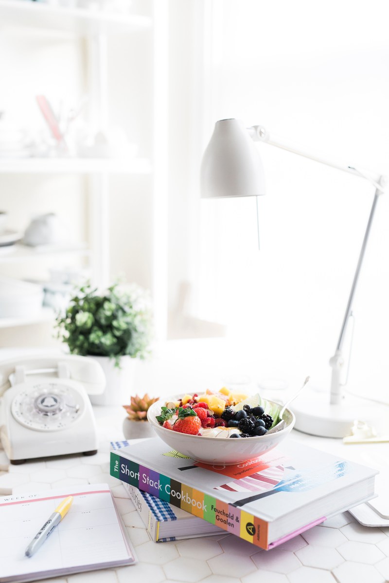 a fruit salad in a bowl on top of a colorful cookbook on a desk, new years resolutions 4k