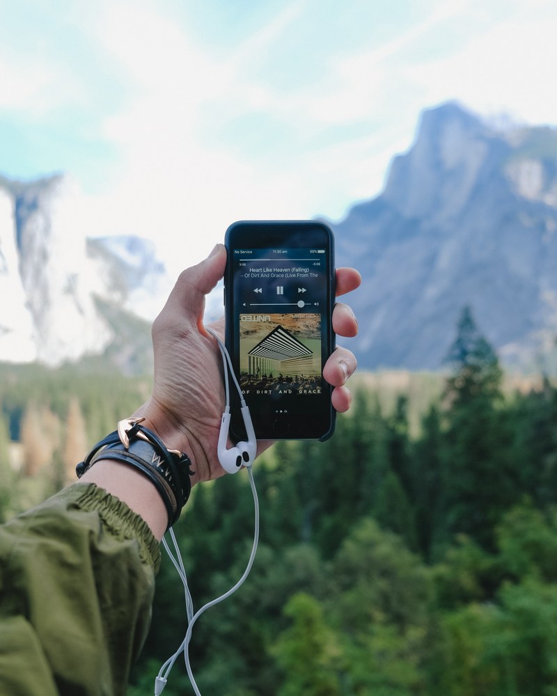 a persons outstretched hand holding an iphone with a music player in the yosemite valley, iphone music and the yosemite valley 4k