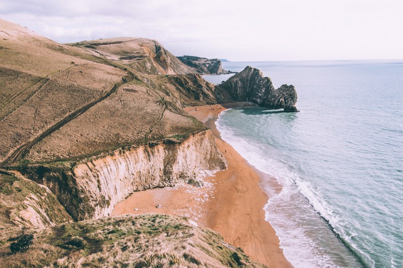 drone view of the coastal cliffs above sand beach at durdle door, coastline drone view 4k