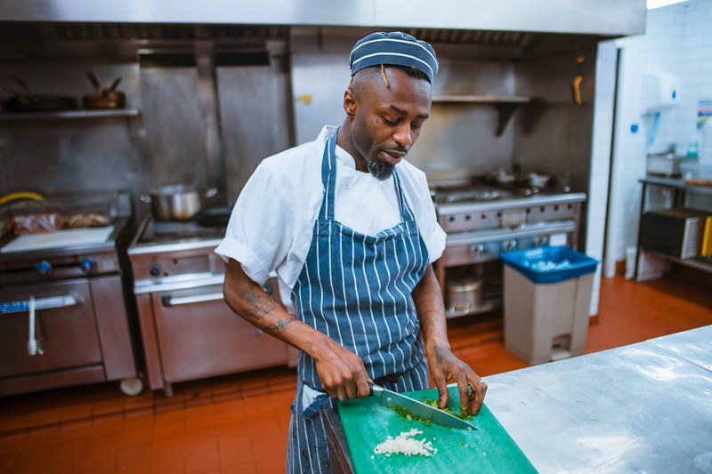 a chef in a blue apron and hat cutting herbs in a kitchen, michael 4k