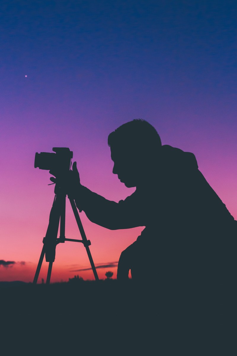a silhouette of a photographer adjusting a camera on a tripod, shoot the sunset 4k
