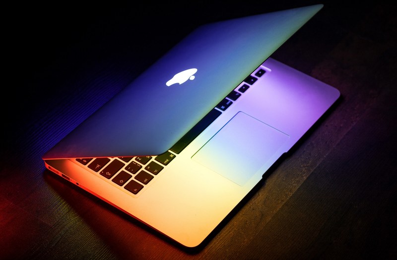 a macbook lit up in rainbow colors on a wooden surface, rainbow macbook 4k