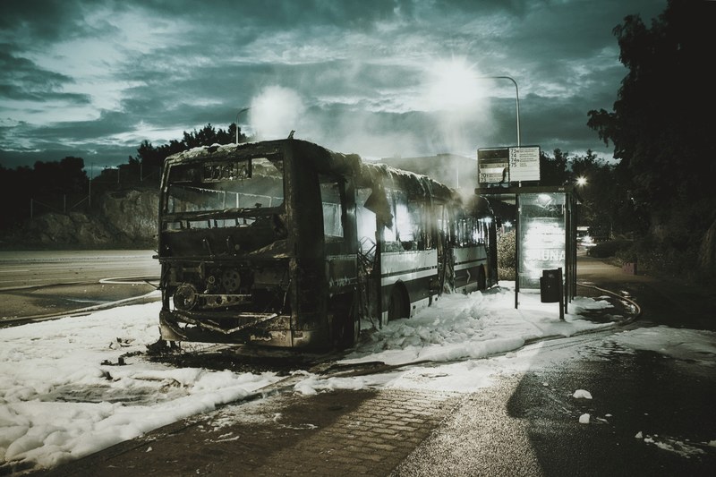 a burnt down bus on a patch of fire fighting foam next to a bus stop, bus fire 4k