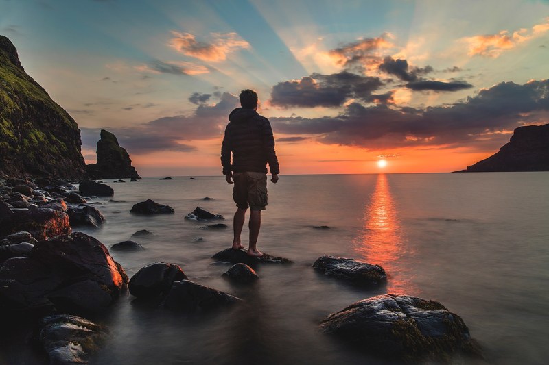 silhouette of man in jacket standing on ocean rock as set sun sets in horizon in skye, talisker bay on the isle of skye 4k