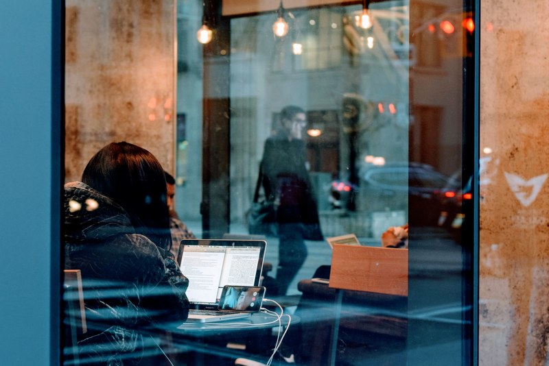 staring into a glass window from a street in toronto at a female looking at her phone and computer, looking at computer and phone 4k