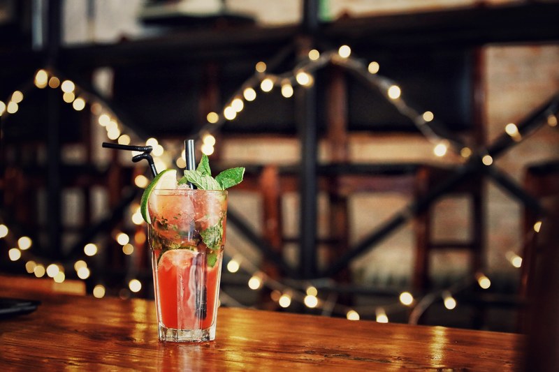 a garnished cocktail beverage with straw and fairy lights behind it, cocktail beverage with straw 4k