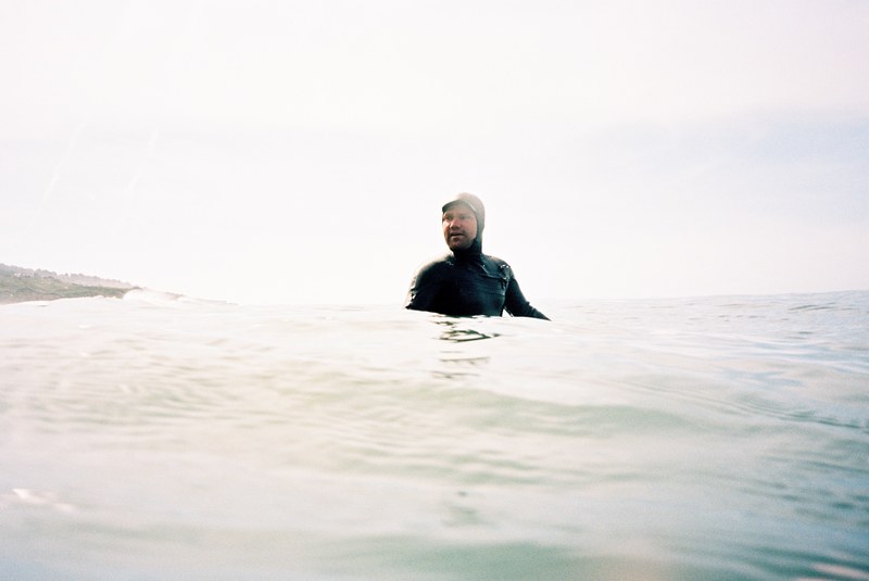 a surfer wearing a wetsuit which comes over his head popping up amidst the waves at santa cruz, glassy mornings 4k