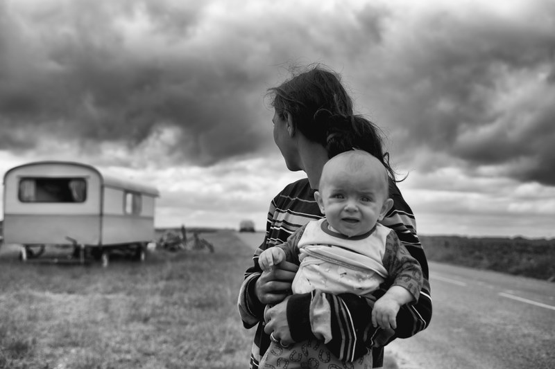 black and white image of a mother holding a child next to a road and trailer, la pita des roms 4k