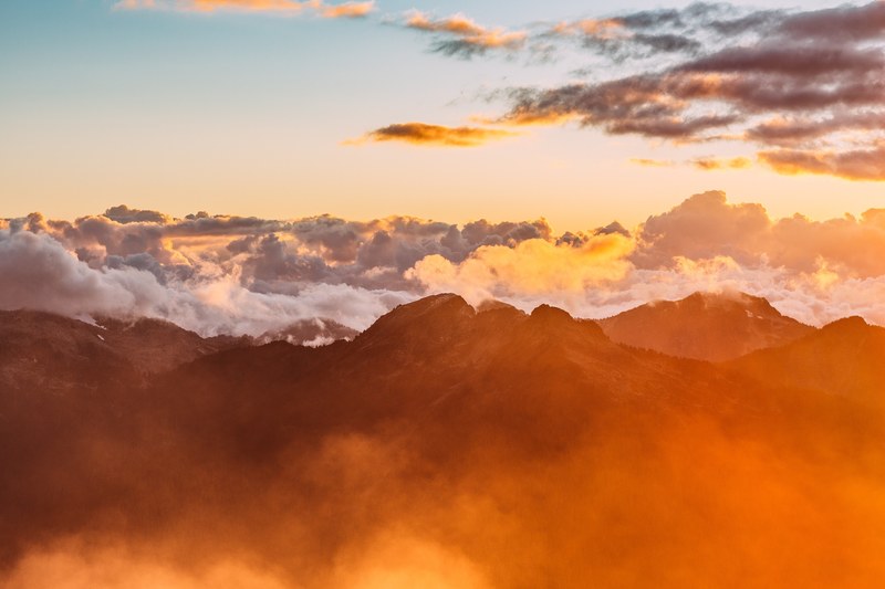 clouds envelop a mountain range during sunset, orange clouds over mountains 4k