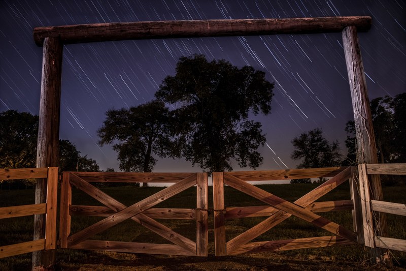 an archway with a gated fence in lebanon featuring blurry star trails in the background, star trails over a lebanon ranch 4k