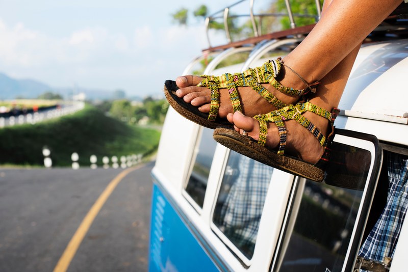 a persons feet in sandals dangling off from the roof of an old van, sitting on a van on the roadside 4k