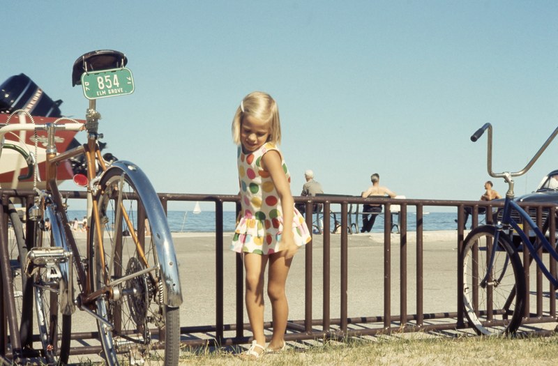 blonde kid girl poses for a shot beside bike while holding the railing in a summer day, blonde girl in summer pose beside bike 4k