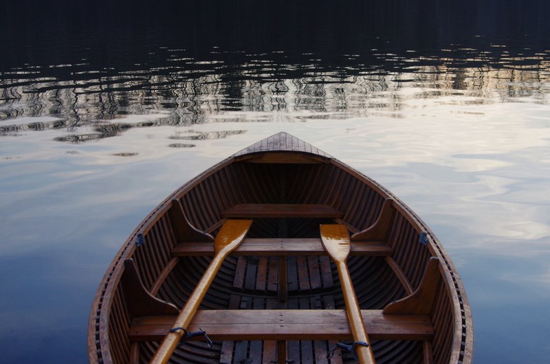 the inside of a small wooden boat on water with two oars, boat on calm water 4k