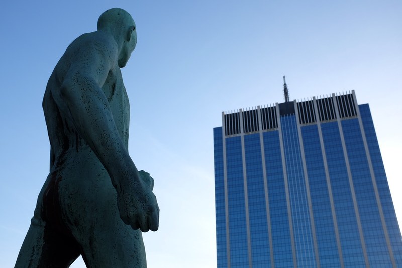 statue of muscular naked man looking at corporate skyscraper in bruxelles, monument in front of building 4k