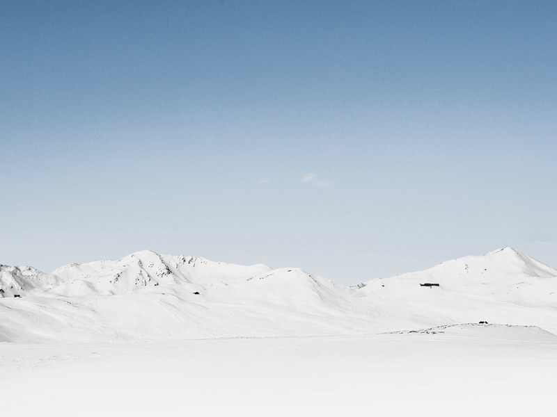 a mountain ridge under a snow blanket on a cloudless day, white mountains under pale blue sky 4k