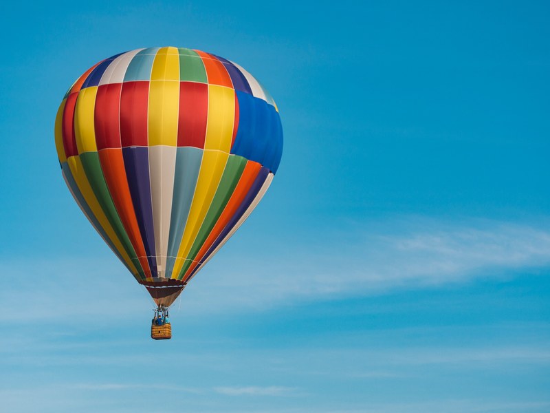three people in the basket of a colorful hot air balloon floating against a blue sky, hot air balloon on blue sky 4k