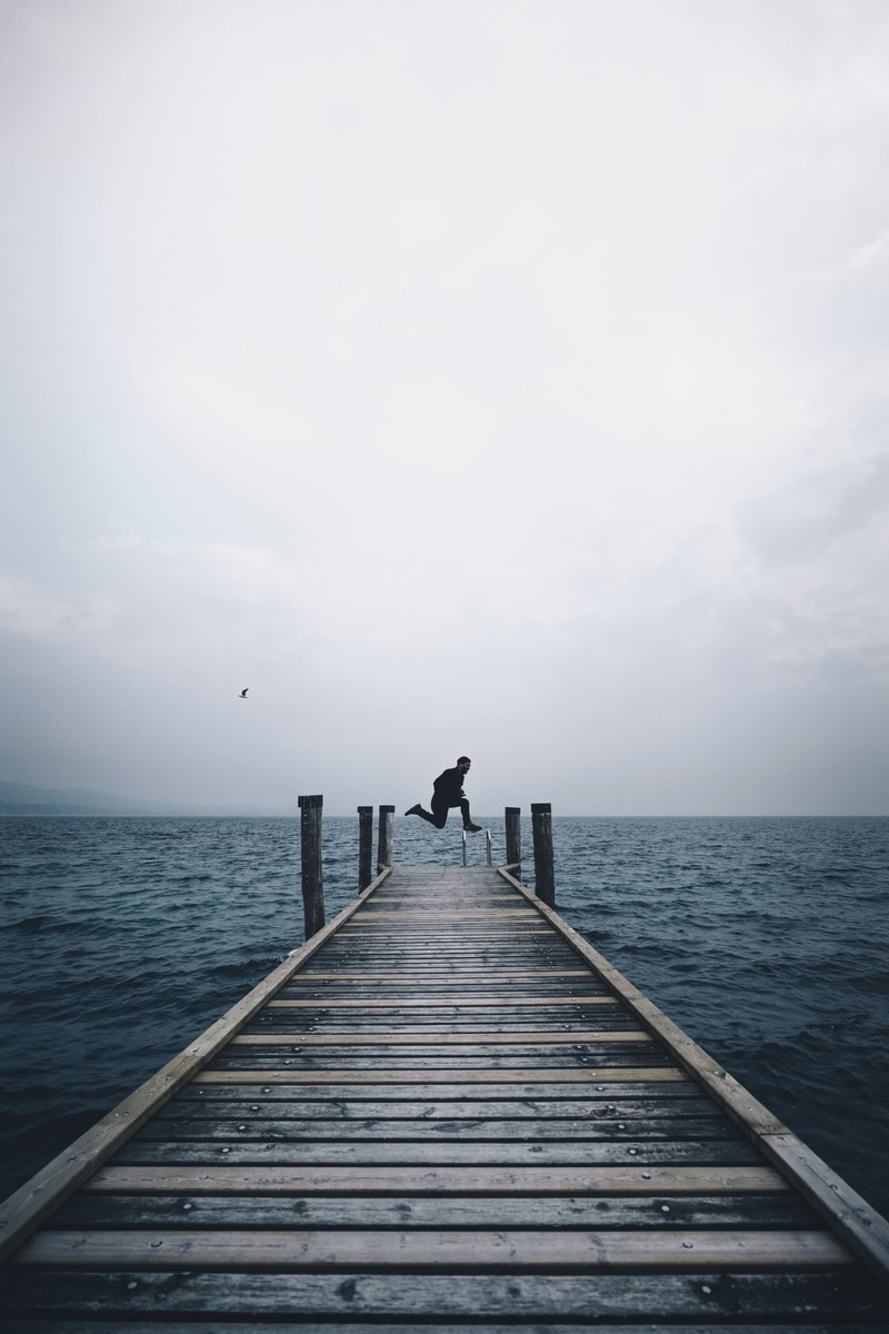 a person jumping in the air on the edge of a dock by a lake in punta saint vigilio on a cloudy day, punta saint vigilio dock jumps 4k