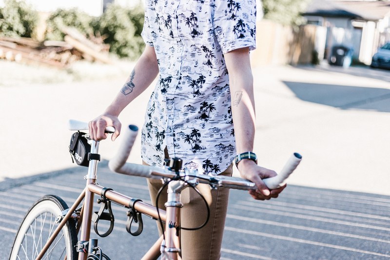 man with tattoos wearing a fashionable pattern shirt holding his golden bike in the afternoon, cyclist standing on the street 4k