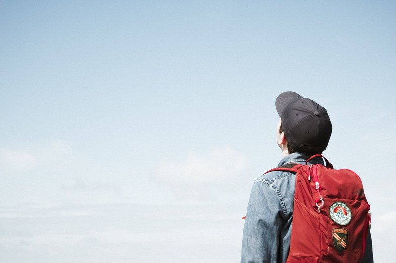 the back view of a man wearing a baseball cap jean jacket and a backpack looking out, man looking out 4k