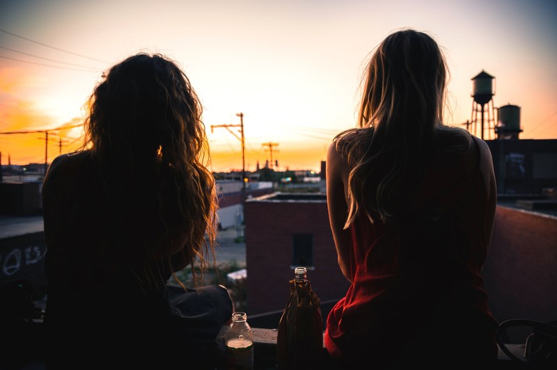 silhouettes of two women sitting on a rooftop watching the sunset, rooftop hangout 4k