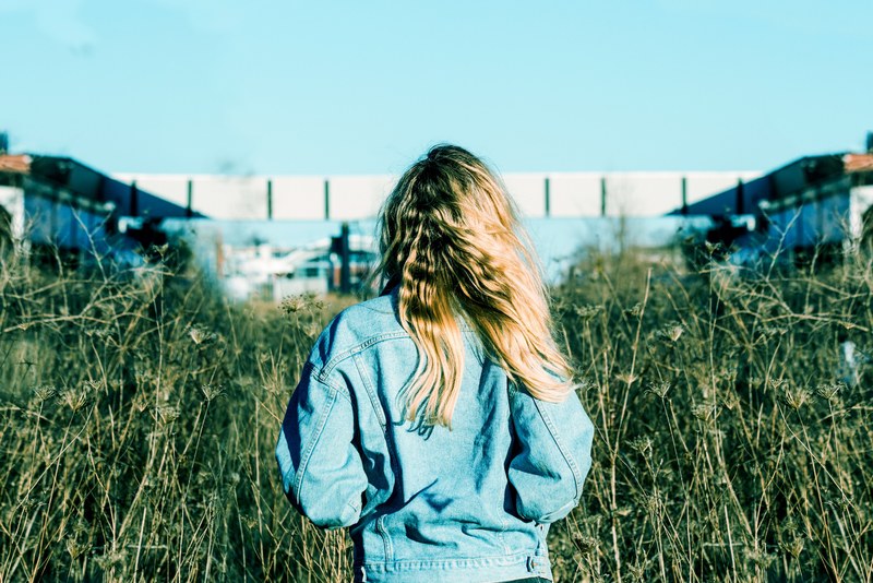 a woman faces away toward a tall green field and buildings in windsor, woman facing a field 4k
