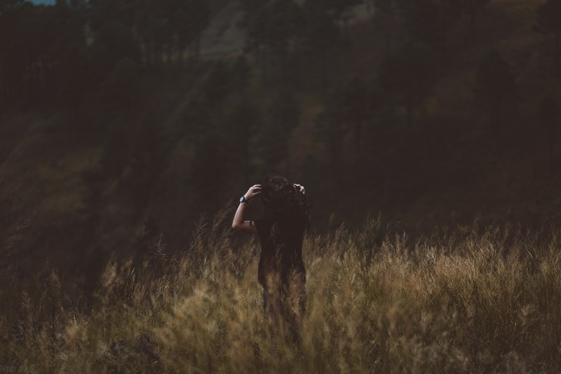 a brunette woman standing in a field and brushing back her hair, black haired woman in a field 4k
