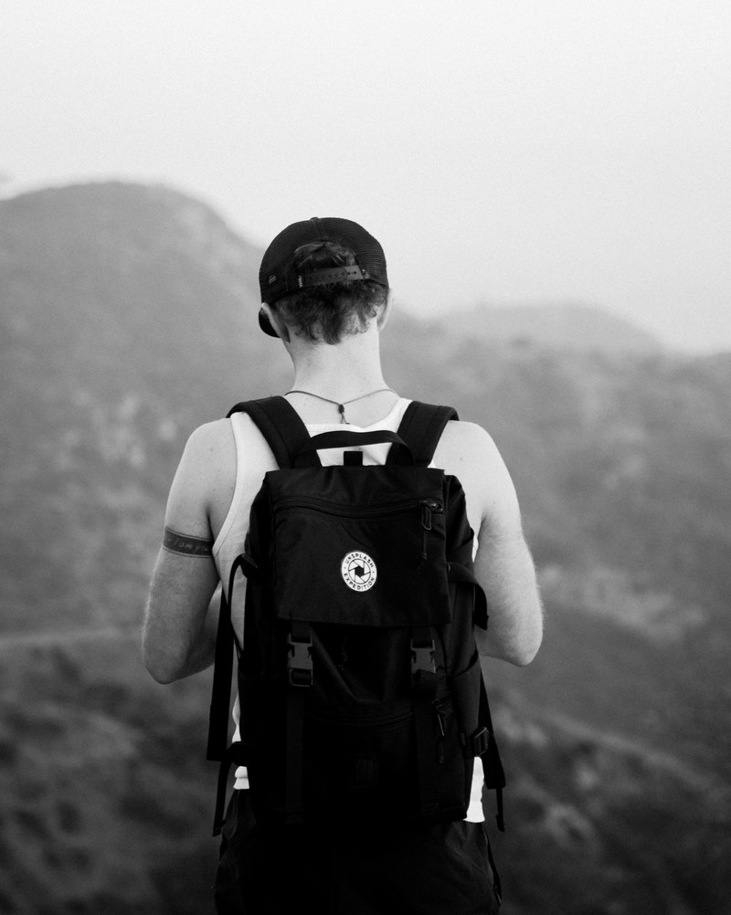 a man wearing a rucksack and baseball cap standing on top of a mountain near hollywood, man on hollywood mountain 4k