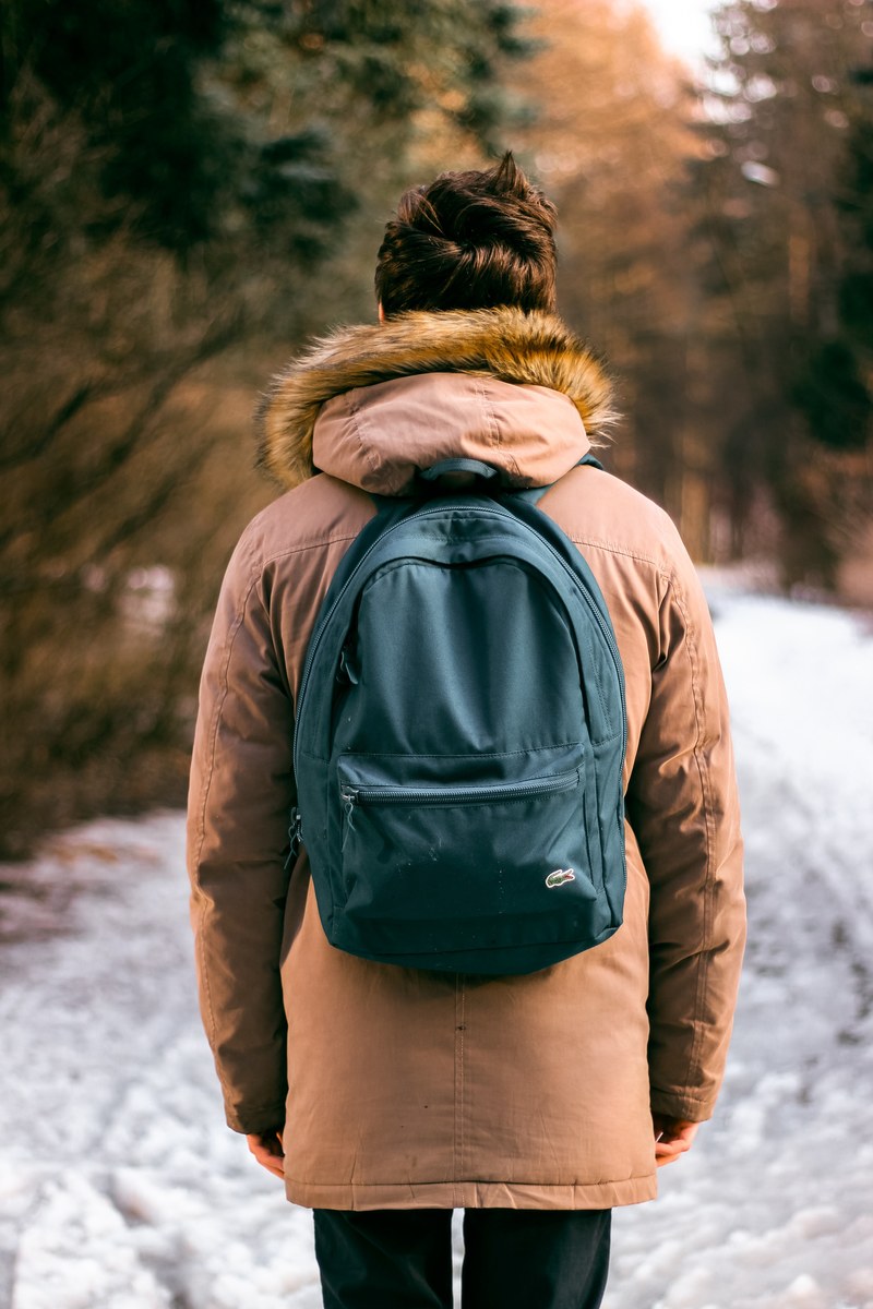 a shot from behind a man wearing lacoste and carrying a backpack down a trail, hiking in lacoste 4k