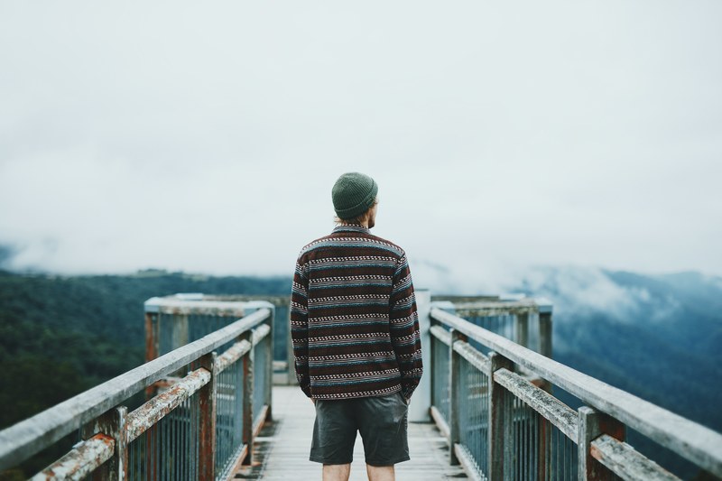 a man in a beanie on an observation deck looking off into the distance, man on a mountain bridge 4k