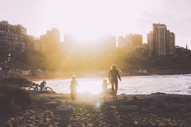 a mother holds her childs hand and another follows behind as they walk towards the shore, _sunset across the inlet 4k