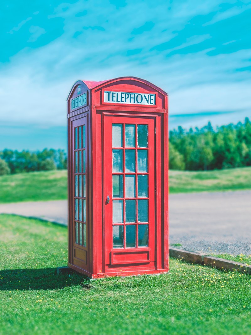 a red telephone booth sits on green grass against a blue sky, telephone booth in grass 4k