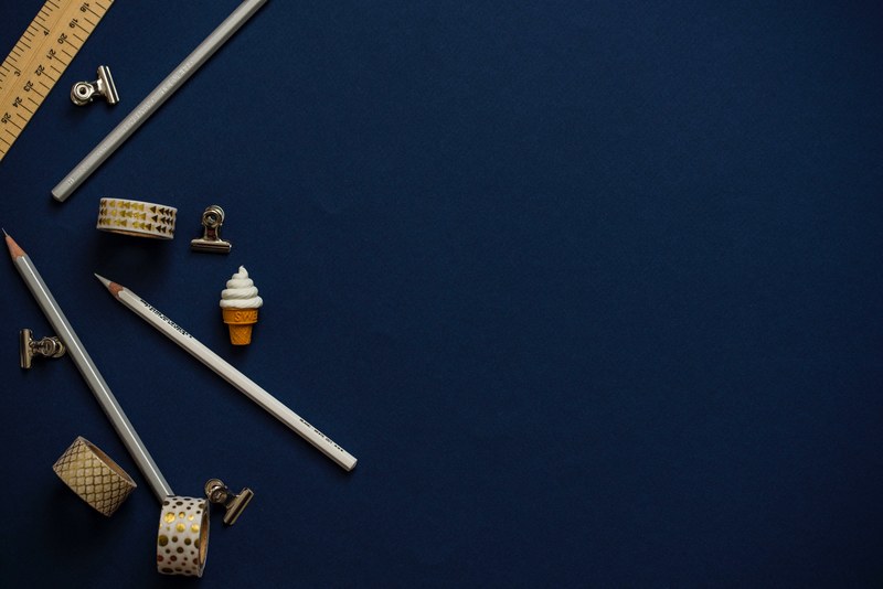 an overhead shot of pencils a ruler scotch tape and bulldog clips on a dark blue surface, coloured pencils 4k
