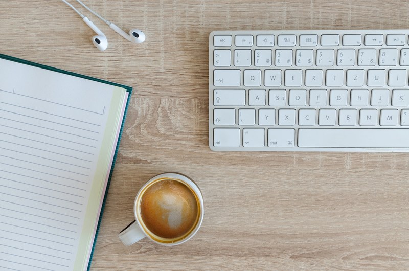 an overhead shot of a cup of coffee a notebook and a keyboard on a wooden desk, workplace in my office with coffee 4k