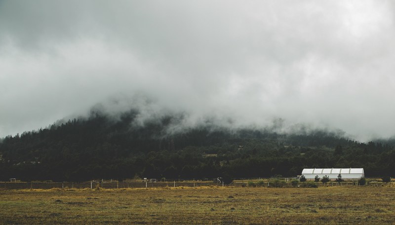 a white building on a field near a fog shrouded hill, field by a misty hill 4k