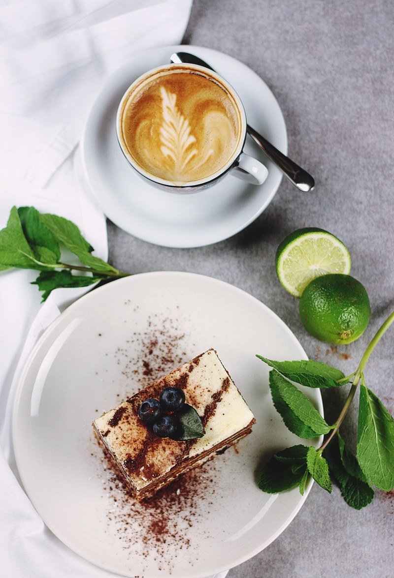 coffee in white cup with foam artwork near plate with cake with dusting mint and lime, coffee and cake artwork 4k