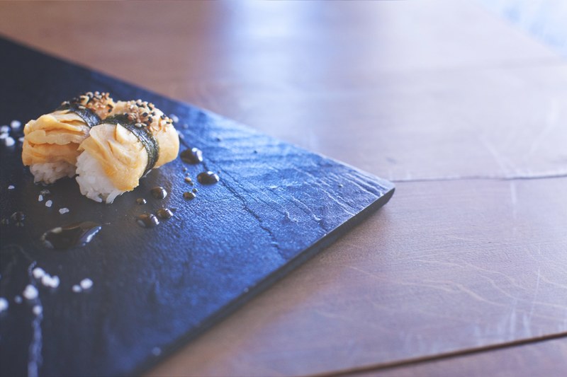 a close up of a set of salmon sushi on a stone plate drizzled with sauce, _sashimi rolls 4k