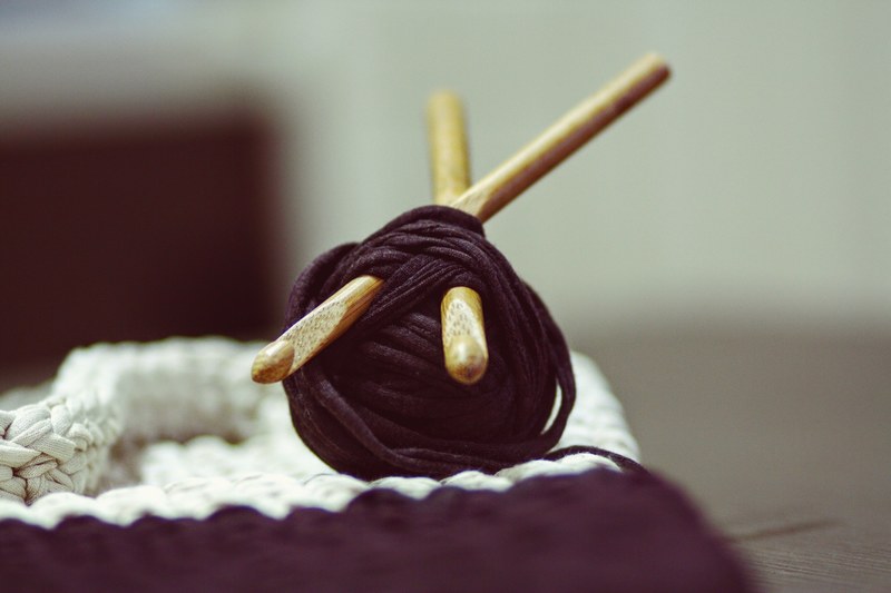 a roll of yarn with wooden knitting needles pierced through next to a weaved fabric, knitting needles and yarn 4k