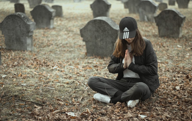 a woman sitting and praying in a cemetery, _praying cemetery 4k
