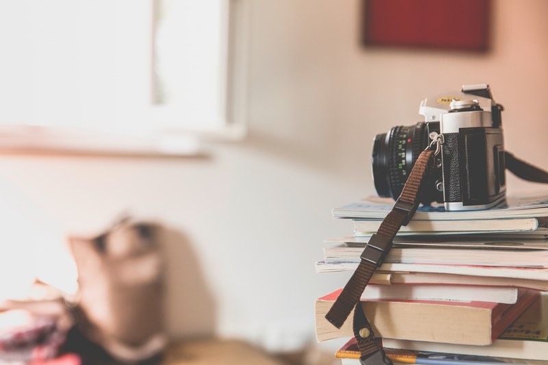 a camera with strap and lens sits on top of a stack of books and magazines, camera on stack of books 4k
