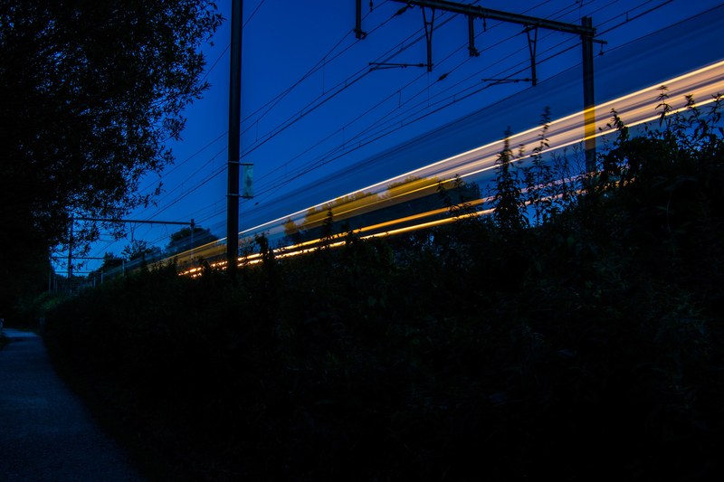 a blurred moving train on a railroad in an early night sky in jette, train track light trail in jette 4k