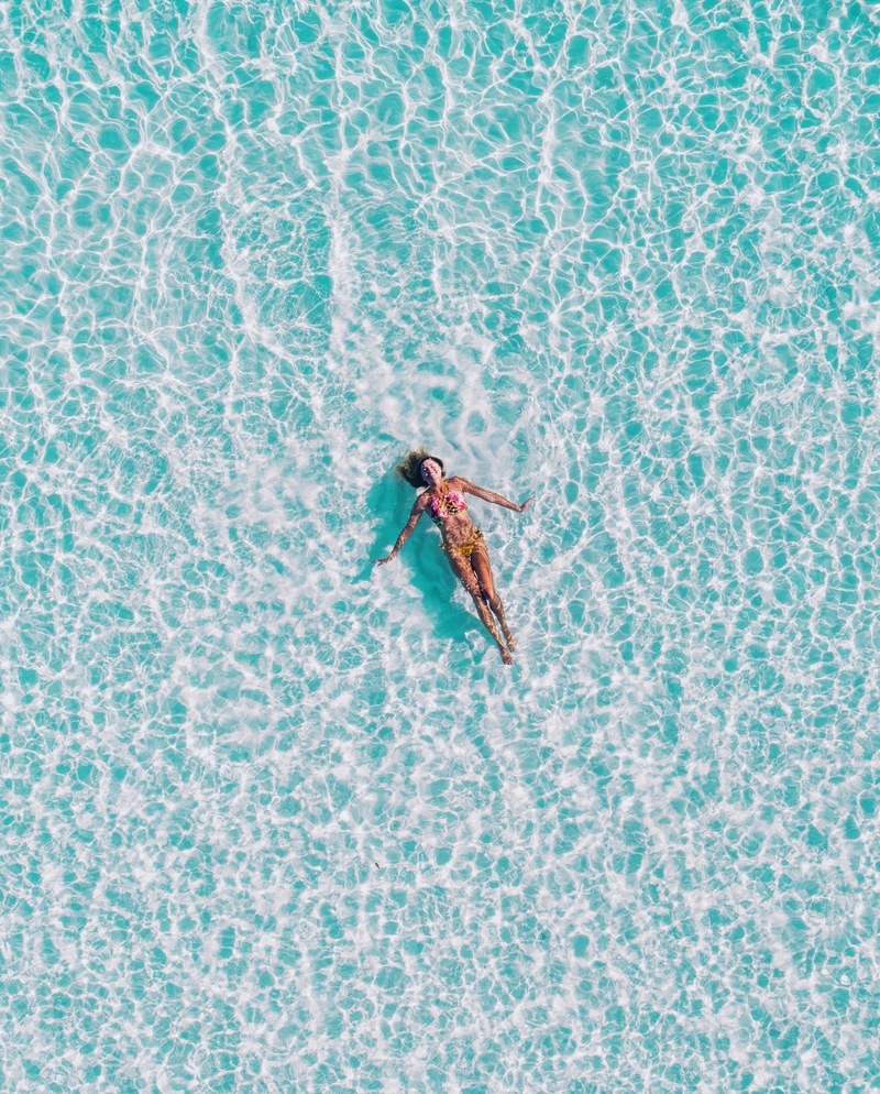 a top view of a woman in a bikini swimming on her back in clear ocean water, lost in the turquoise 4k