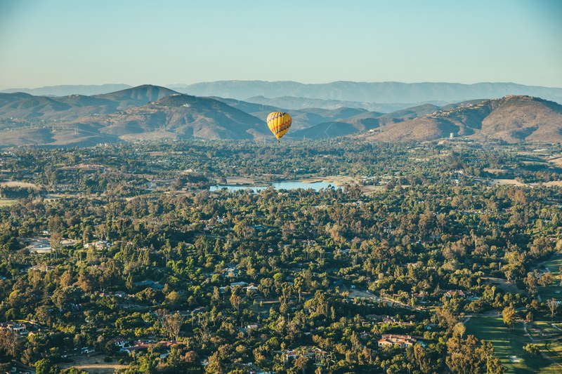 a yellow hot air balloon in the air above a small village among hills, hot air balloon over a village 4k