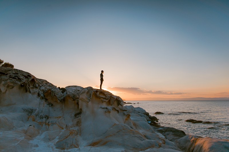 a person standing on large rocks near the ocean, _sunset 4k