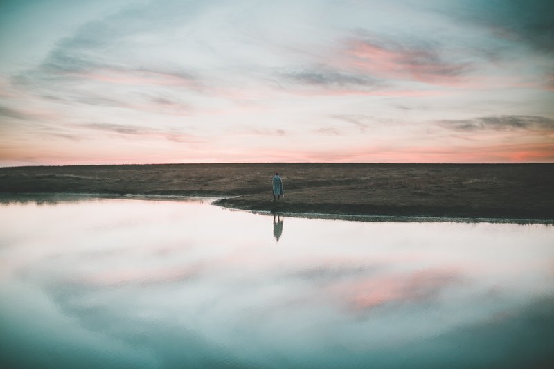 a person in a coat strolling along the shore of a lake, reflection 4k