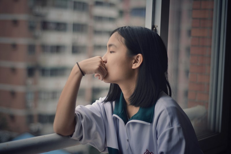 a teenager looks out the window with a hand on mouth and elbows on the railing, _teenage girl window railing 4k