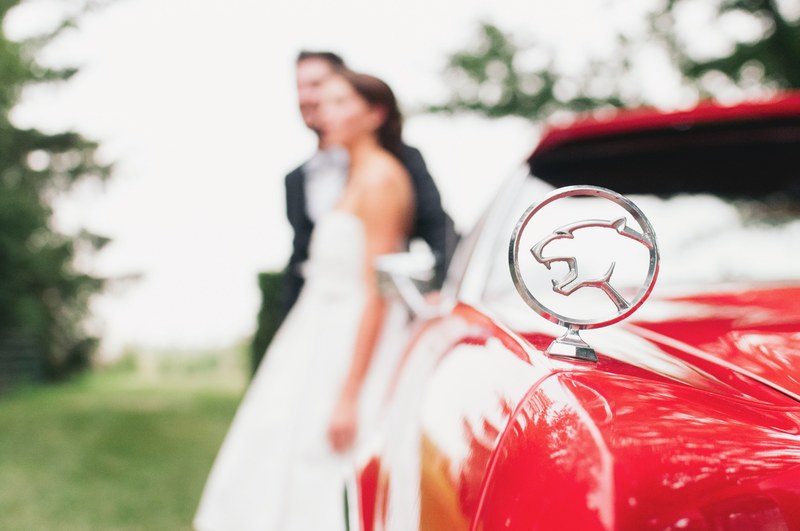 vintage red jaguar car with married couple in background out of focus, wedding with red car 4k