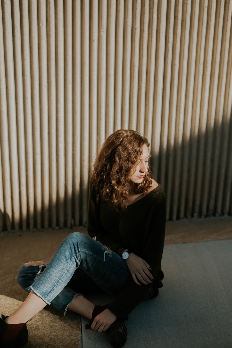 woman sitting alone near a wall half lit half in shadow, sitting in shadow 4k